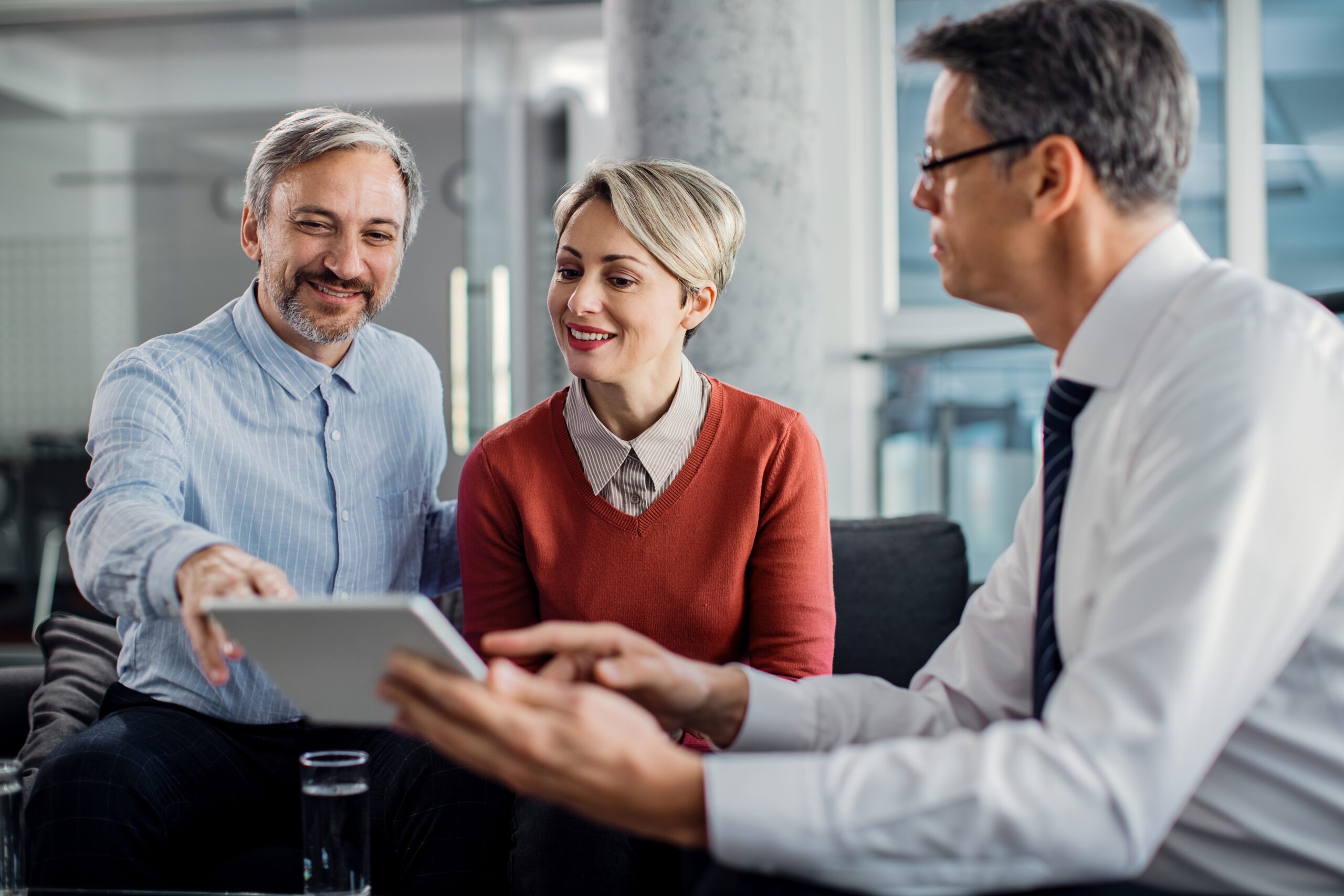 Happy mid adult couple using touchpad with their financial consultant in the office.